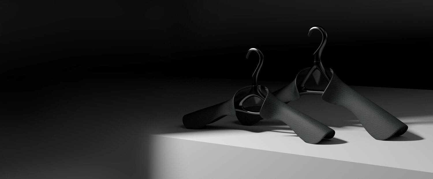Pair of Lou Hansell Matte Black luxury garment hangers in Onyx leather finish, representing refined design and craftsmanship.
