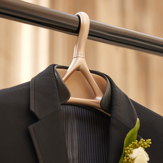 Image of Lou Hansell's H series luxury wedding dress hanger in Yellow Gold and Matte Black hung up on a rail and holding a black suit jacket with a floral boutonnière pinned to it.