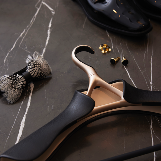Image of Lou Hansell's H series wedding dress hanger with a trouser bar in Yellow Gold and Matte Black laid on a black marble surface next to golden cufflinks and a bowtie.