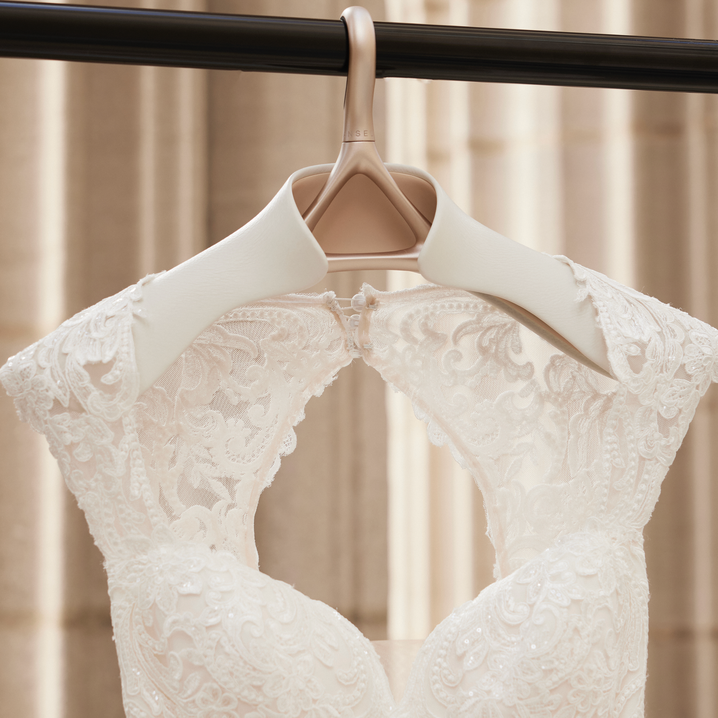 Image of Lou Hansell's H series luxury wedding dress hanger in Yellow Gold and Off-White hung up on a black rail and holding a white wedding dress with lace detailing.