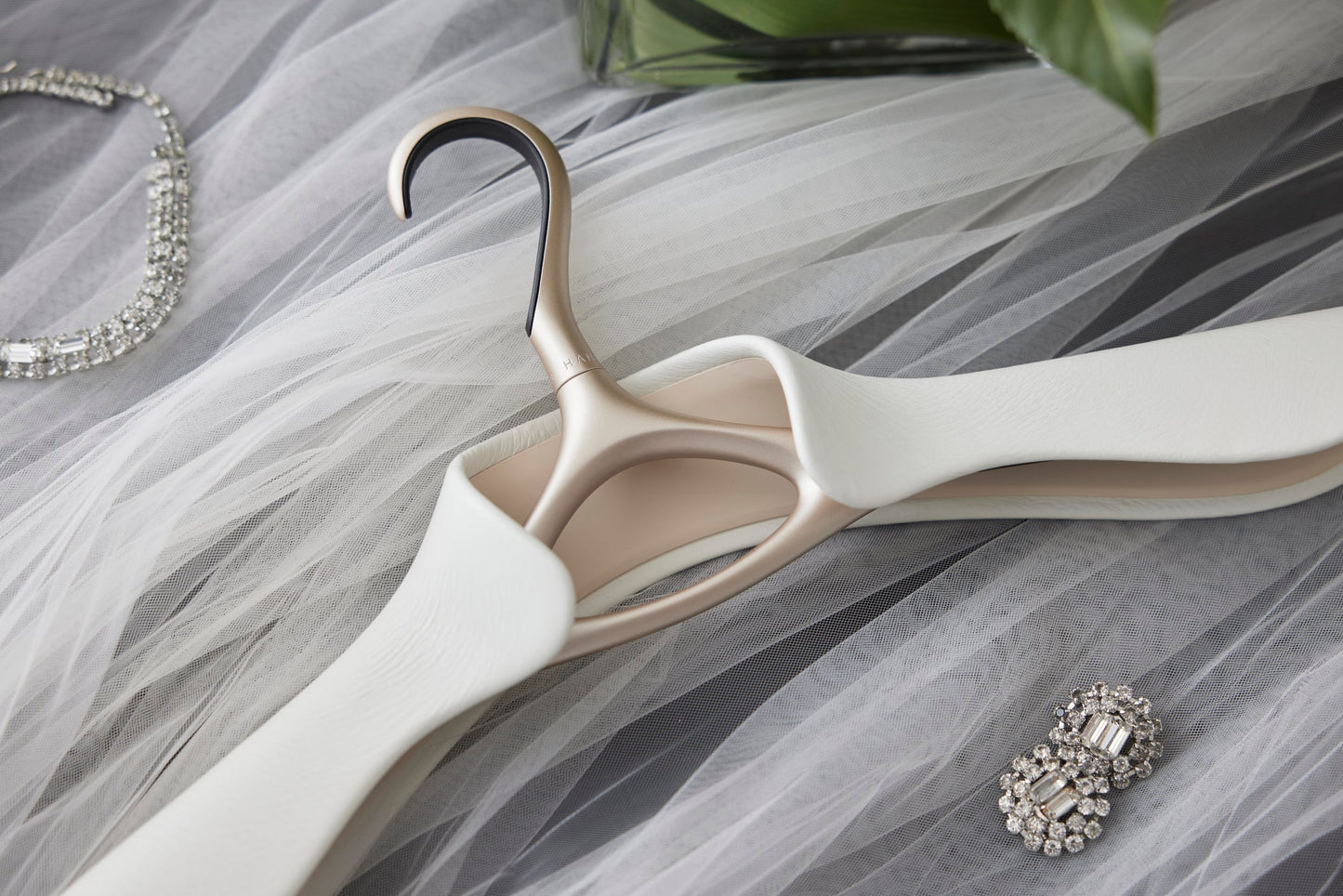 Luxury wedding dress hanger wrapped in off-white Italian leather sitting on tulle with wedding jewelry around it