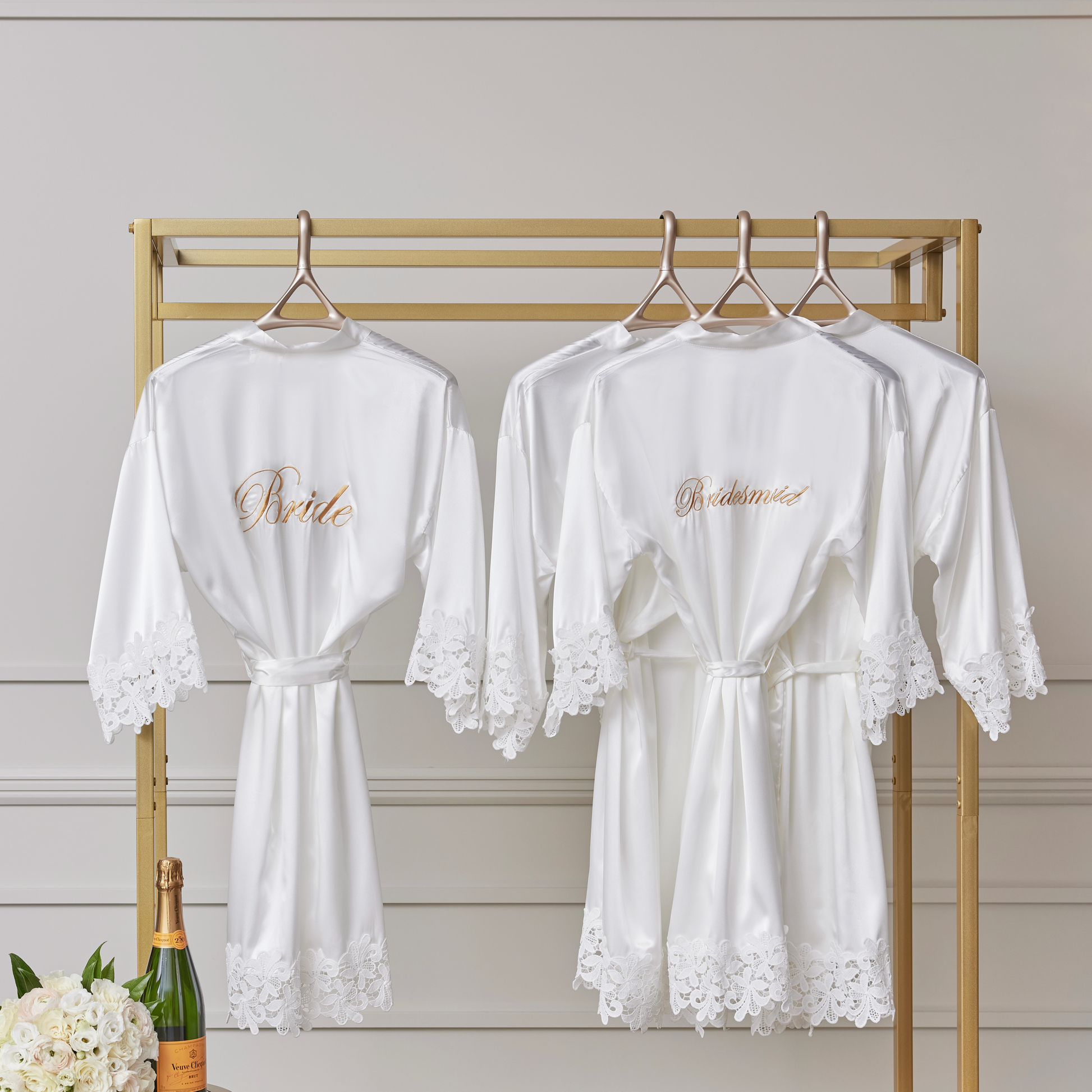 Image of Lou Hansell's H series base bridal wedding hangers in Yellow Gold. They are hung in a line on a golden rail. Each hanger holds a white robe for getting ready on a wedding day.