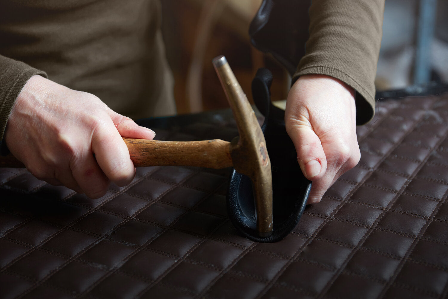Craftsman shaping a Lou Hansell designer hanger using leatherworking tools, highlighting expert craftsmanship and material detail.
