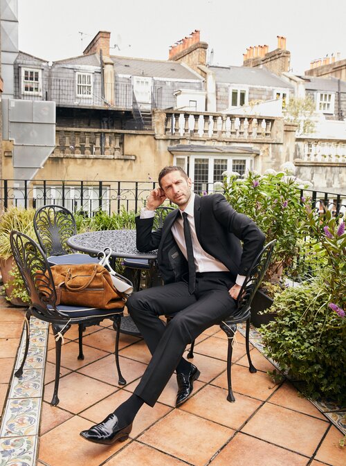Jonathan Heaf seated on a terrace with Lou Hansell garment hangers, embodying refined style and innovative design.
