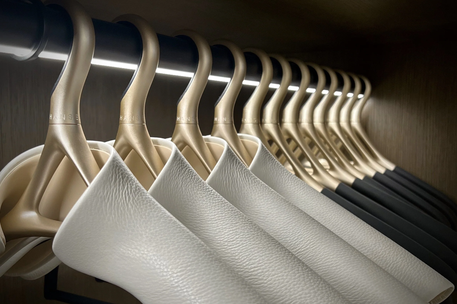Collection of Lou Hansell premium Yellow Gold and Off White Italian leather clothes hangers displayed in a wardrobe, reflecting sustainable craftsmanship and refined luxury.