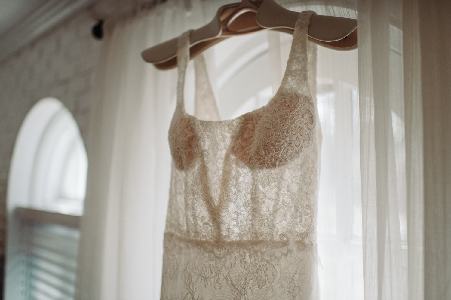 White lace dress hanging in front of a sheer curtain